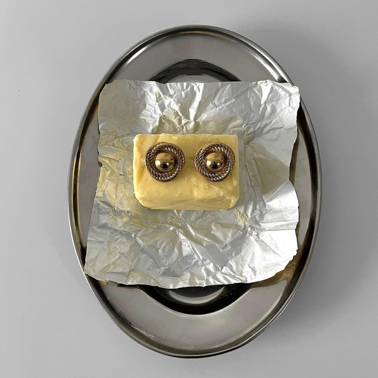 Small gold earring on a piece of tinfoil inside a silver earring holder against a gray background